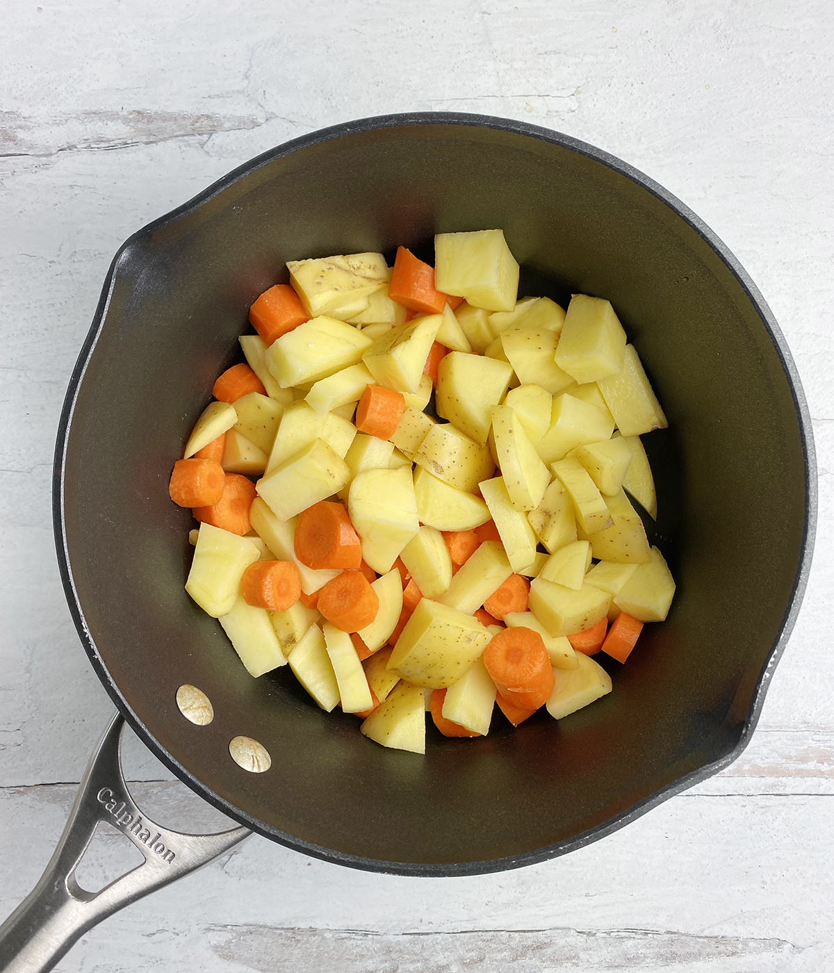 Uncooked carrots and potatoes in a pot.
