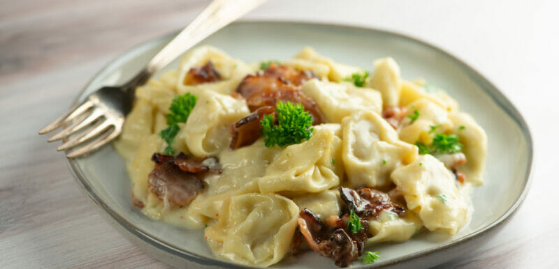 bacon tortellini alfredo on plate with fork