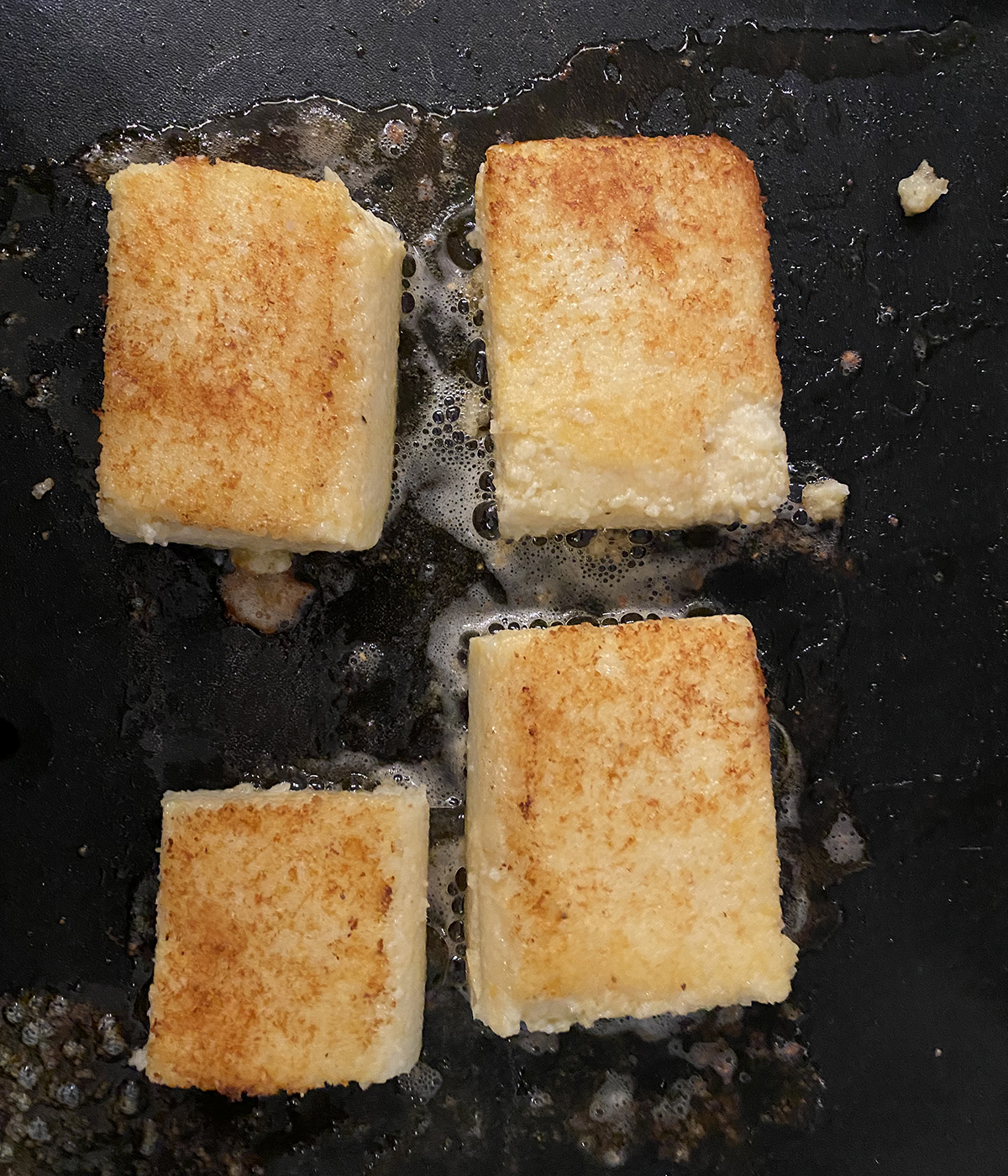 Cheesy Grit Cakes browning on a griddle.