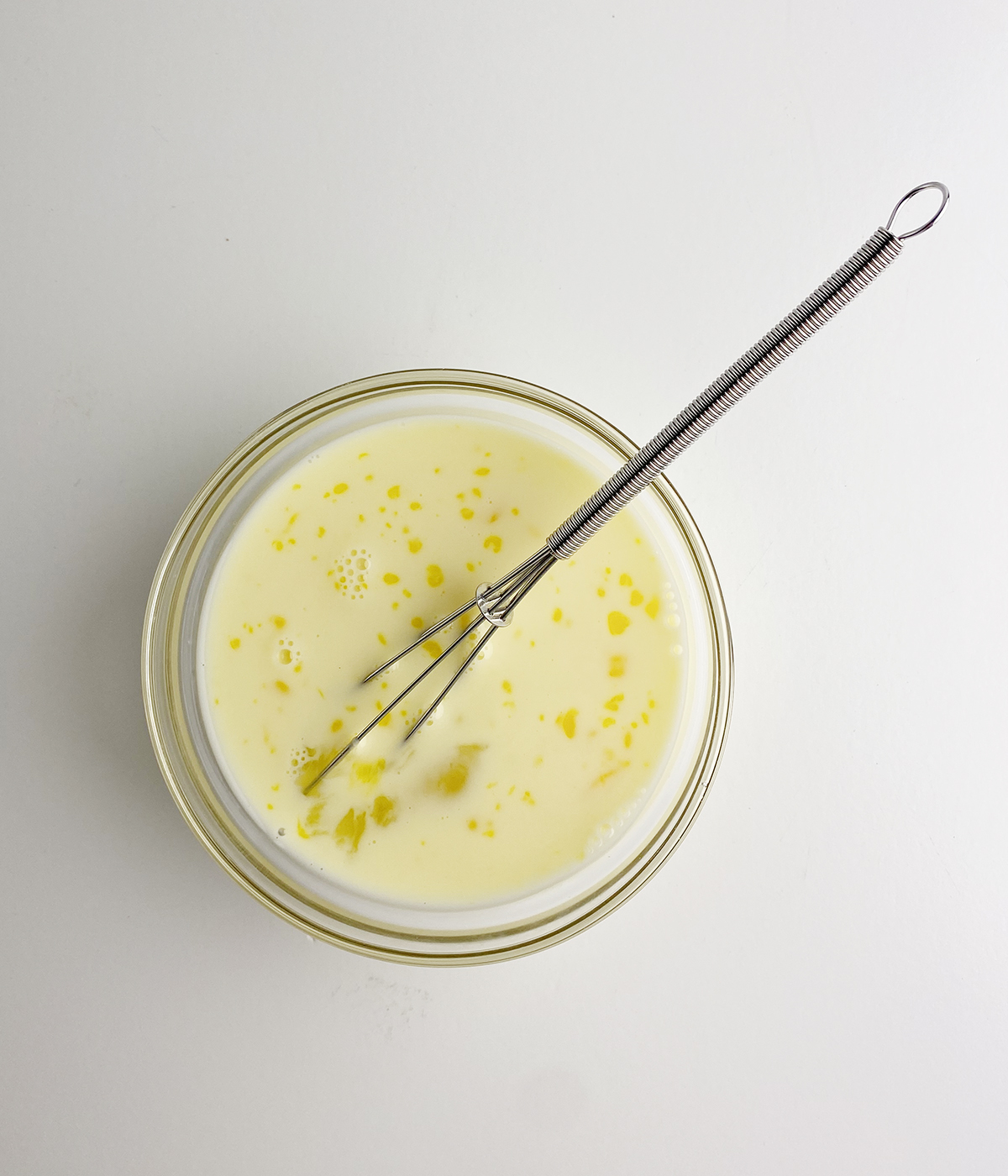 Milk and egg mixture in a bowl with a whisk.