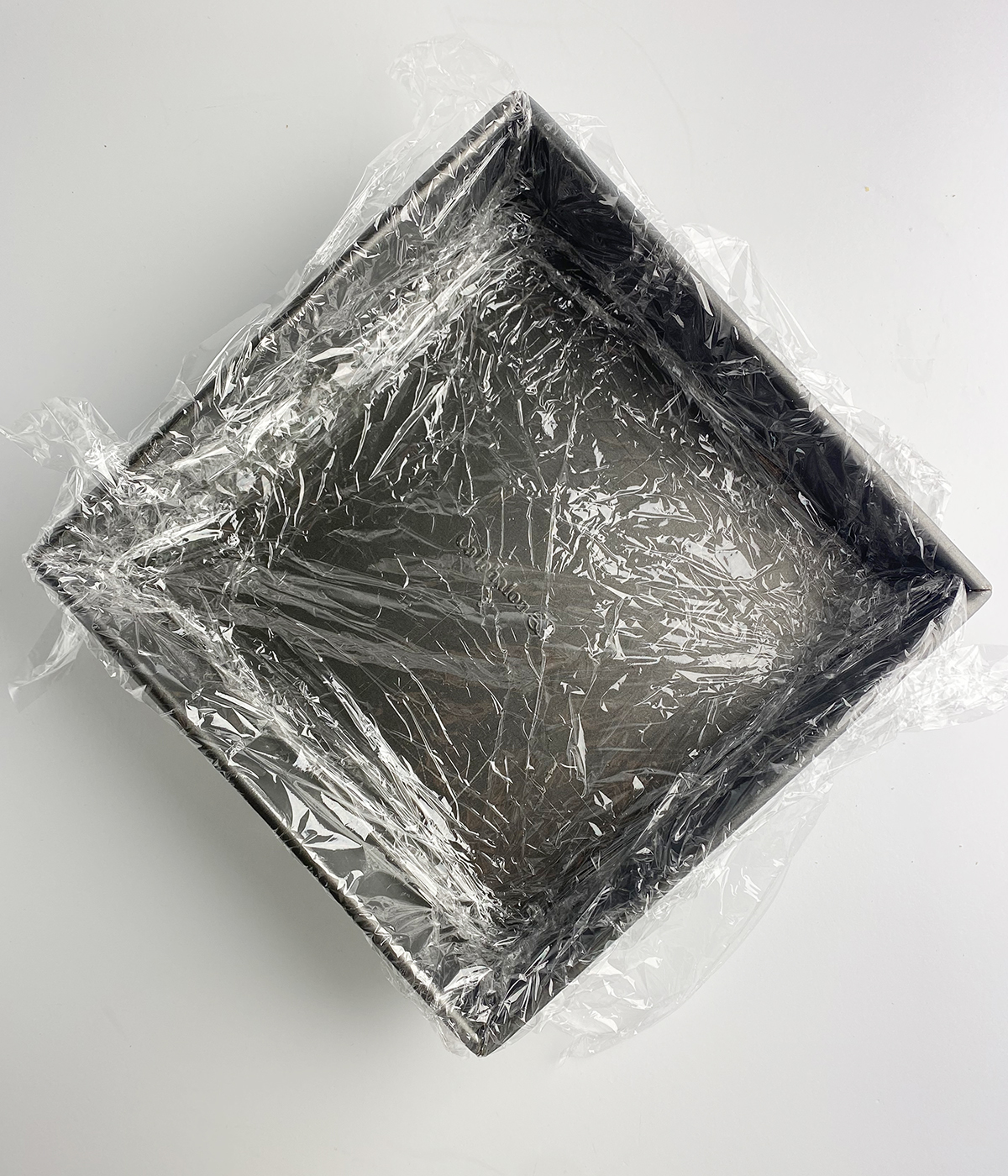 Plastic wrap lining an eight inch square cake pan.