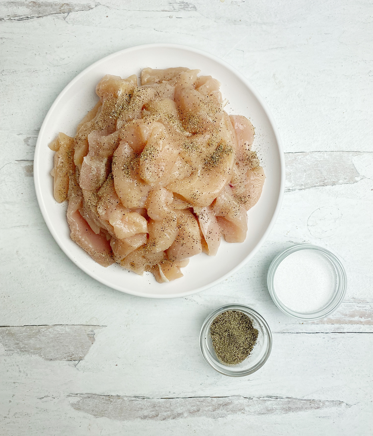 Raw boneless chicken breast pieces in a bowl with salt and pepper.