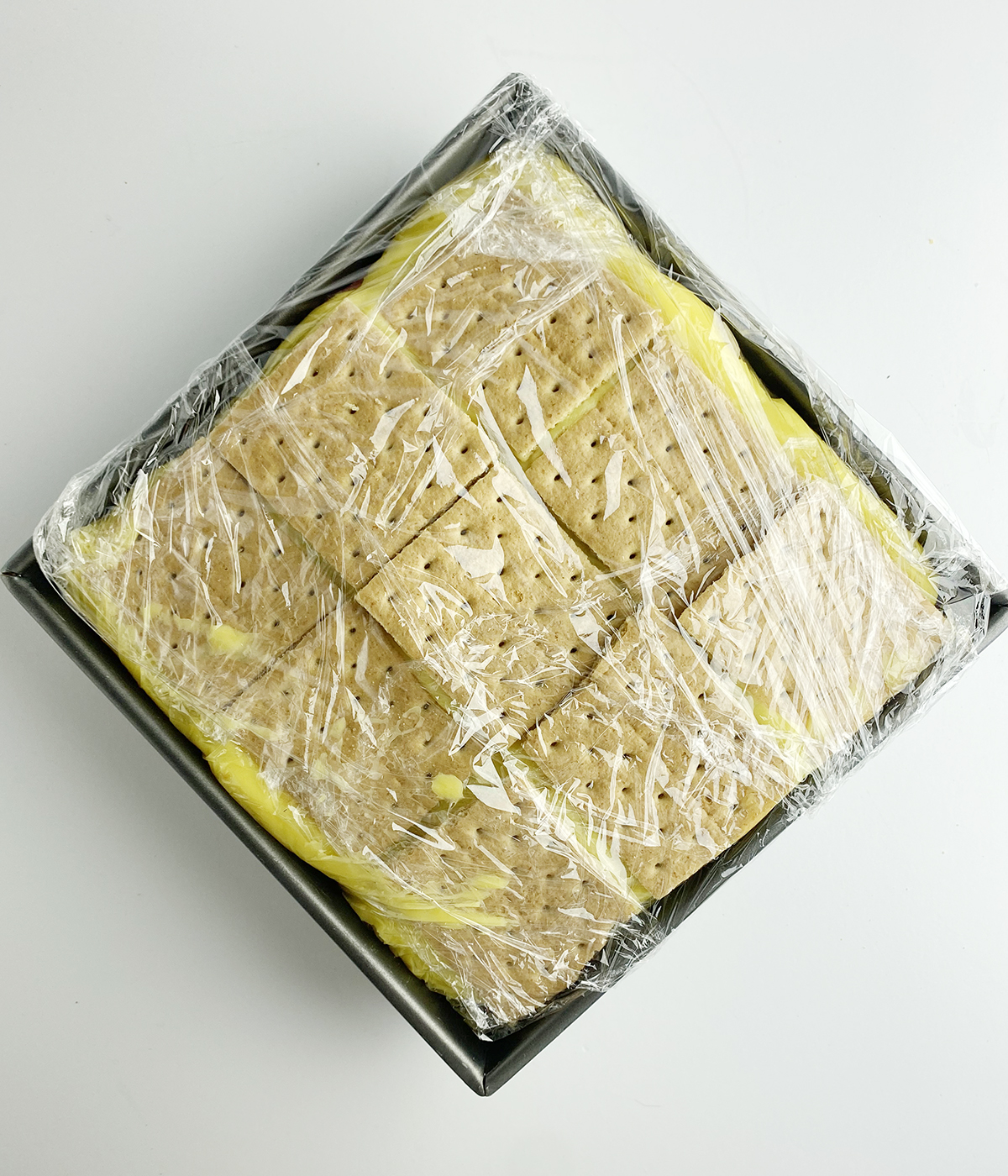 Strawberry banana icebox cake wrapped in plastic wrap.