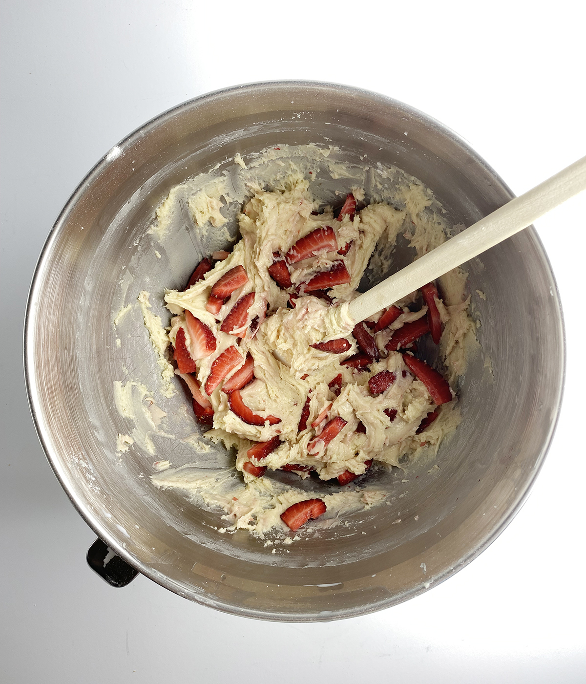 Folding sliced strawberries into strawberry bread batter.