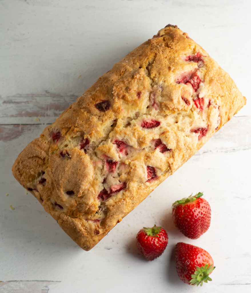 Loaf of strawberry bread with strawberries on the ocunter.
