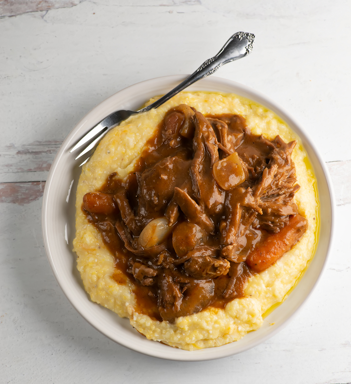 Slow cooker coca cola pot roast over grits on a plate.