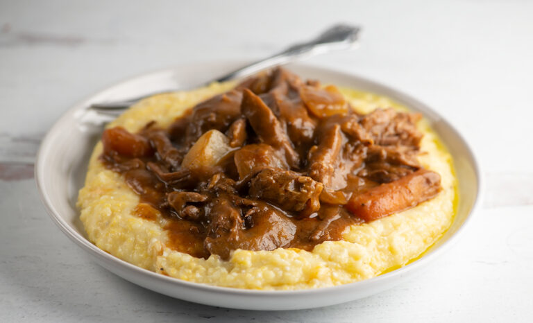 Slow cooker coca cola pot roast on a plate with grits.