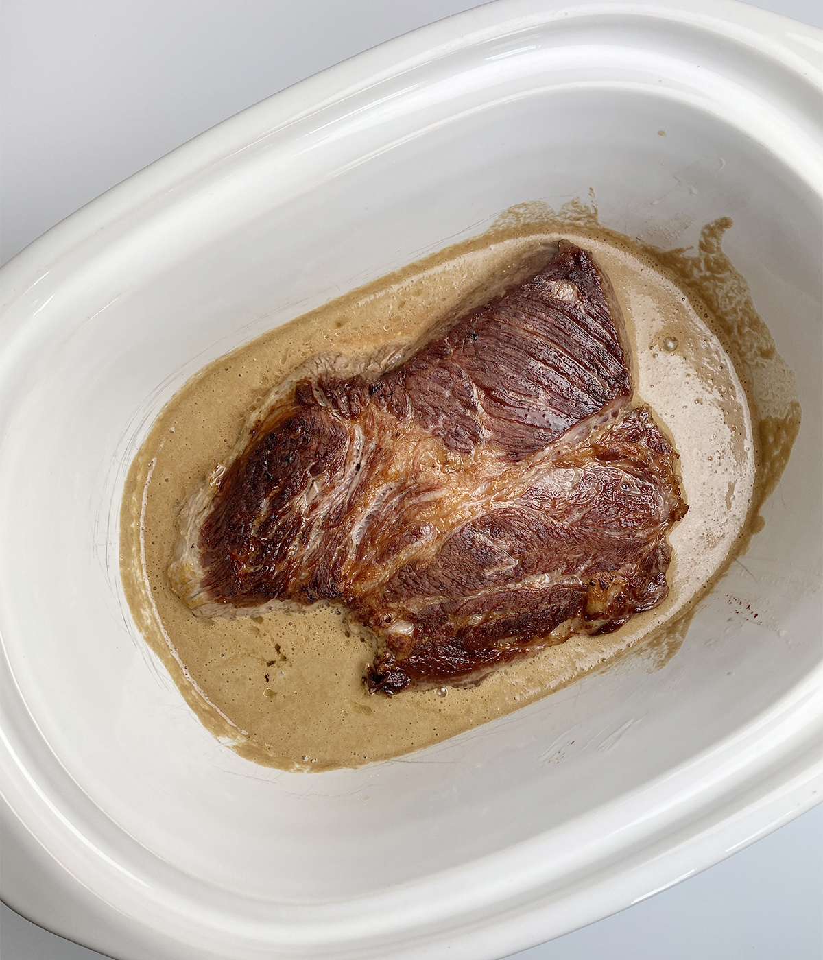 Seared chuck roast and cola sauce in a slow cooker ready to be cooked.