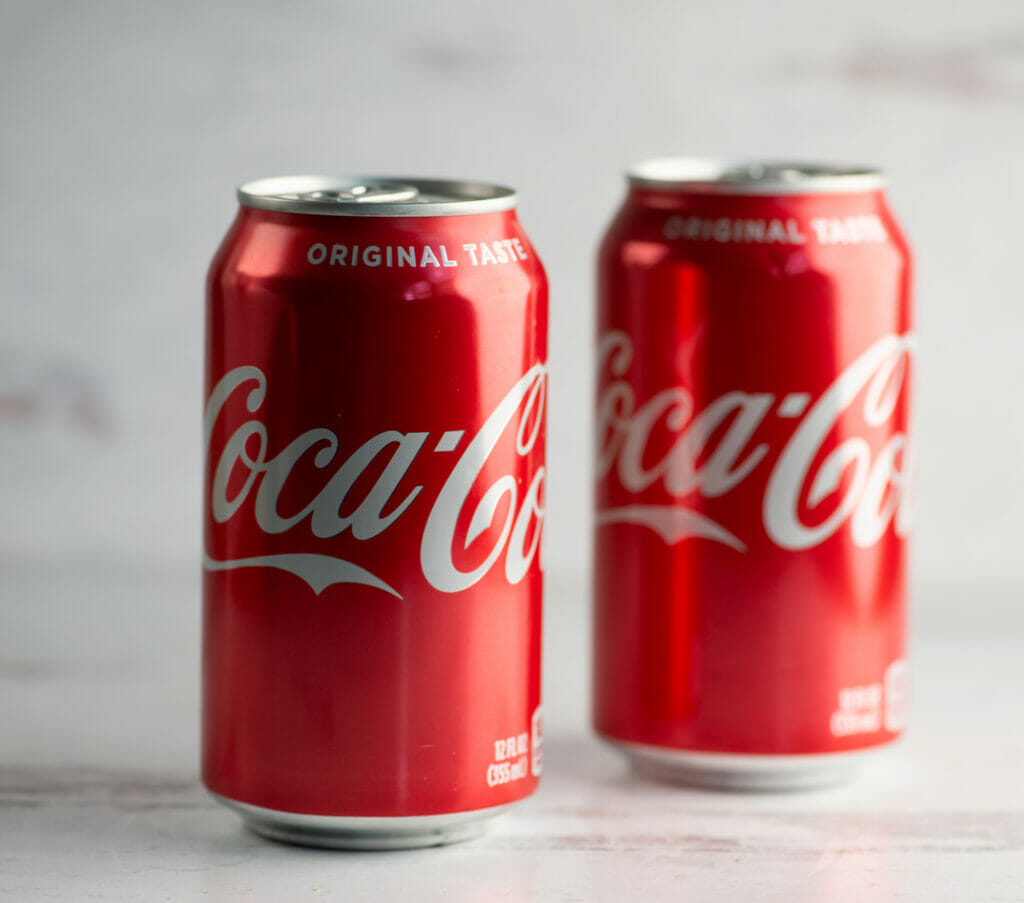 Two cans of Coca-Cola on a wooden counter.