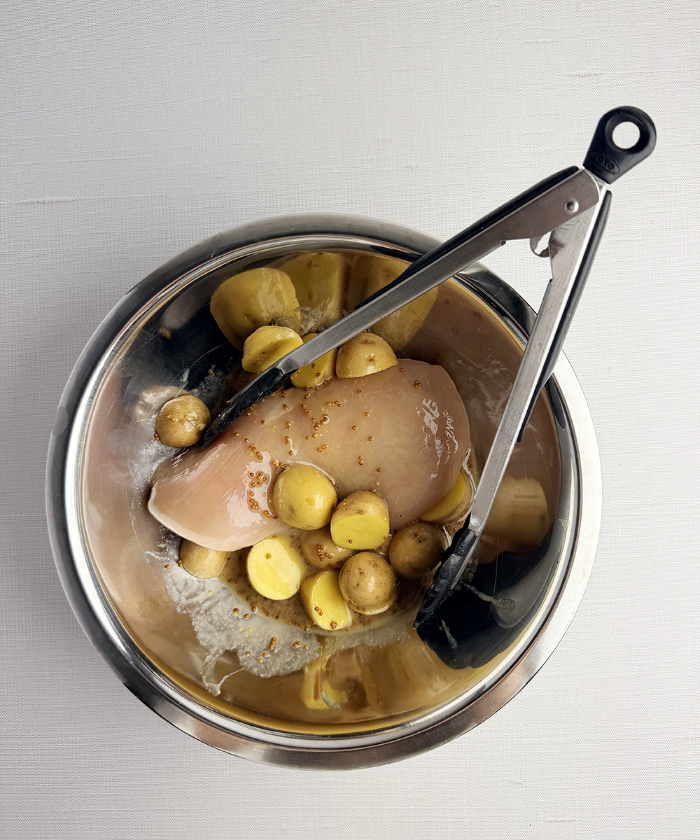 Chicken and potatoes in a mixing bowl with tongs.