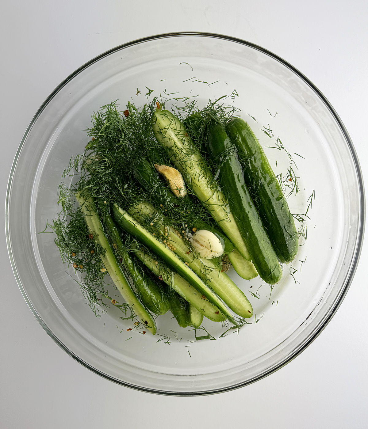 Cucumbers mixed with dill and garlic in a bowl.