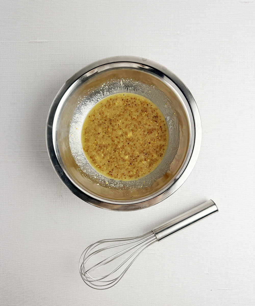 Mustard dressing in a bowl with a whisk.