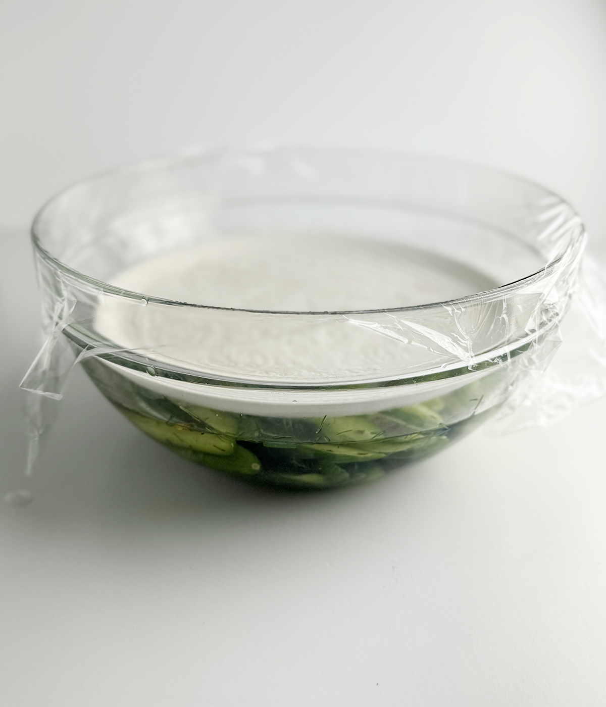 Refrigerator pickles in a bowl with a plate on top.