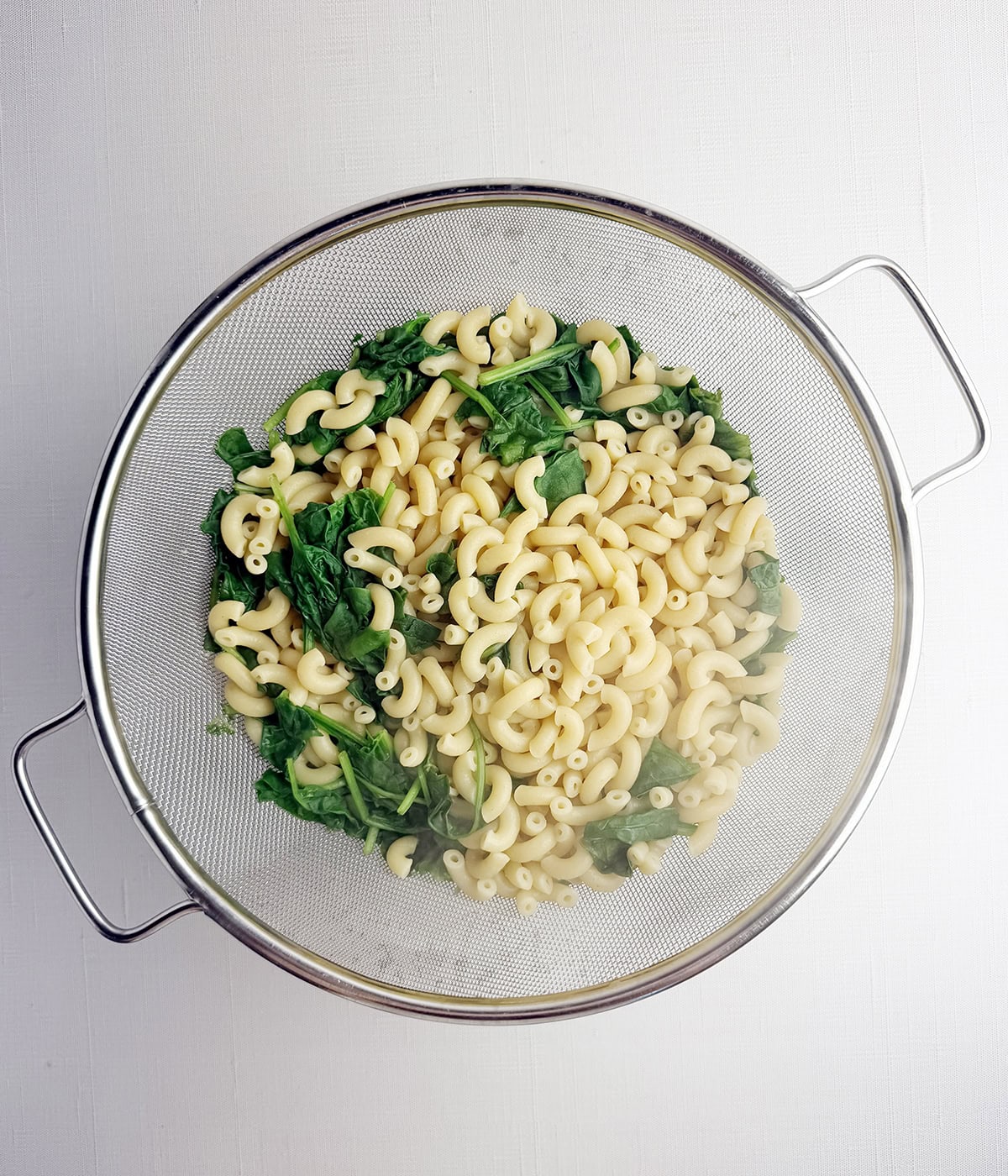 Strainer with elbow macaroni and cooked spinach.