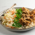 Slow cooker brown sugar pulled chicken on a plate with coleslaw.