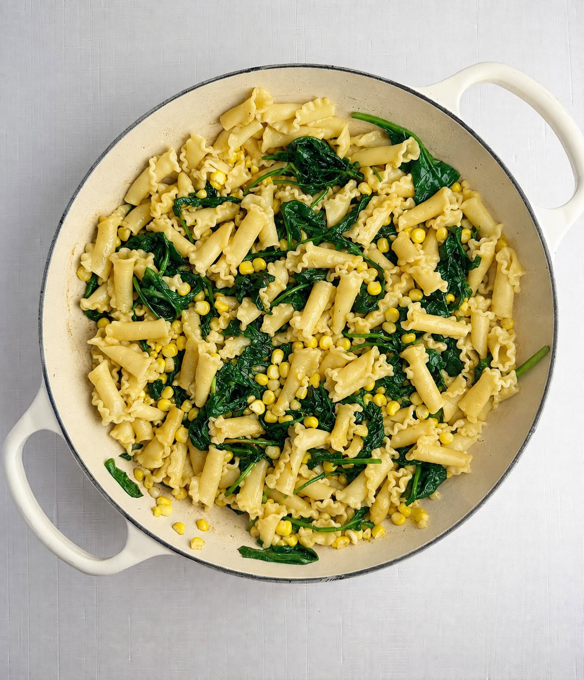 Pasta, corn and spinach in a skillet.