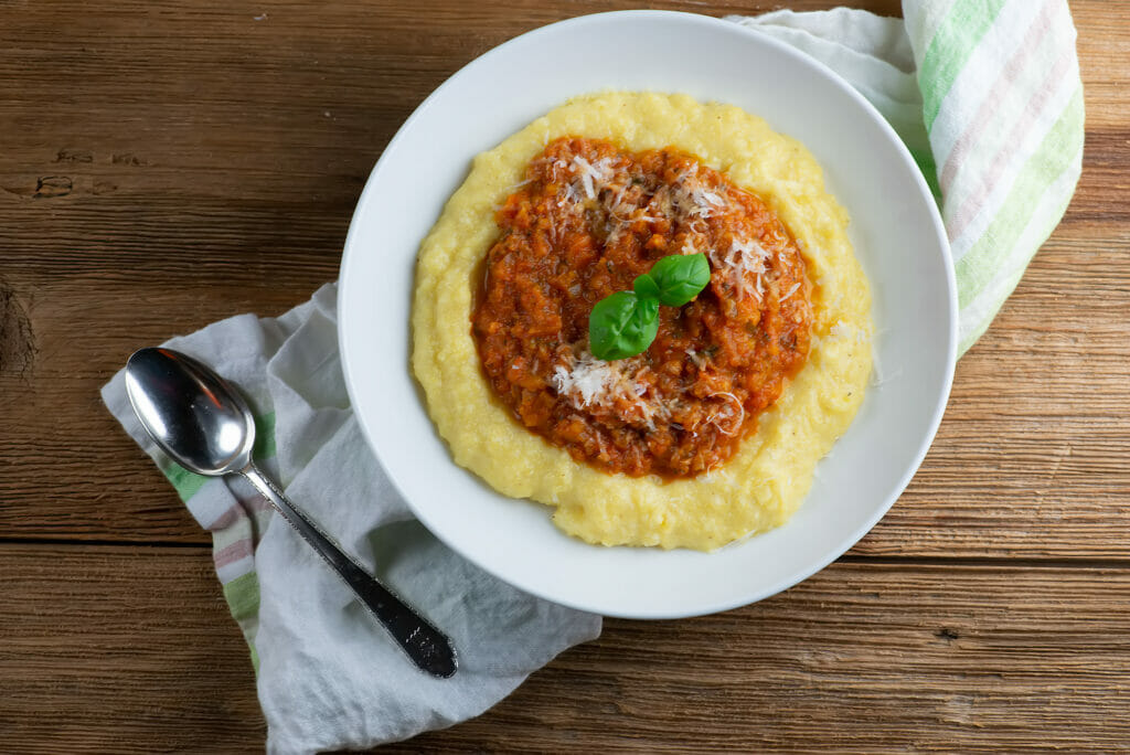 A bowl of polenta with sweet tomato sauce with a spoon.