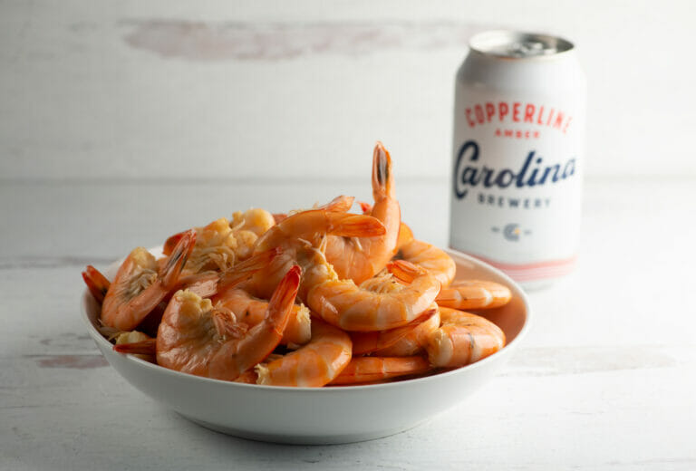 Shrimp cooked in beer in a bowl with a can of beer in the background.