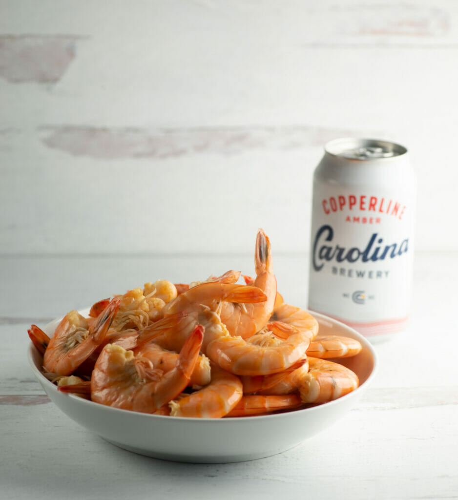 Shrimp cooked in beer in a bowl with a can of beer in the background.