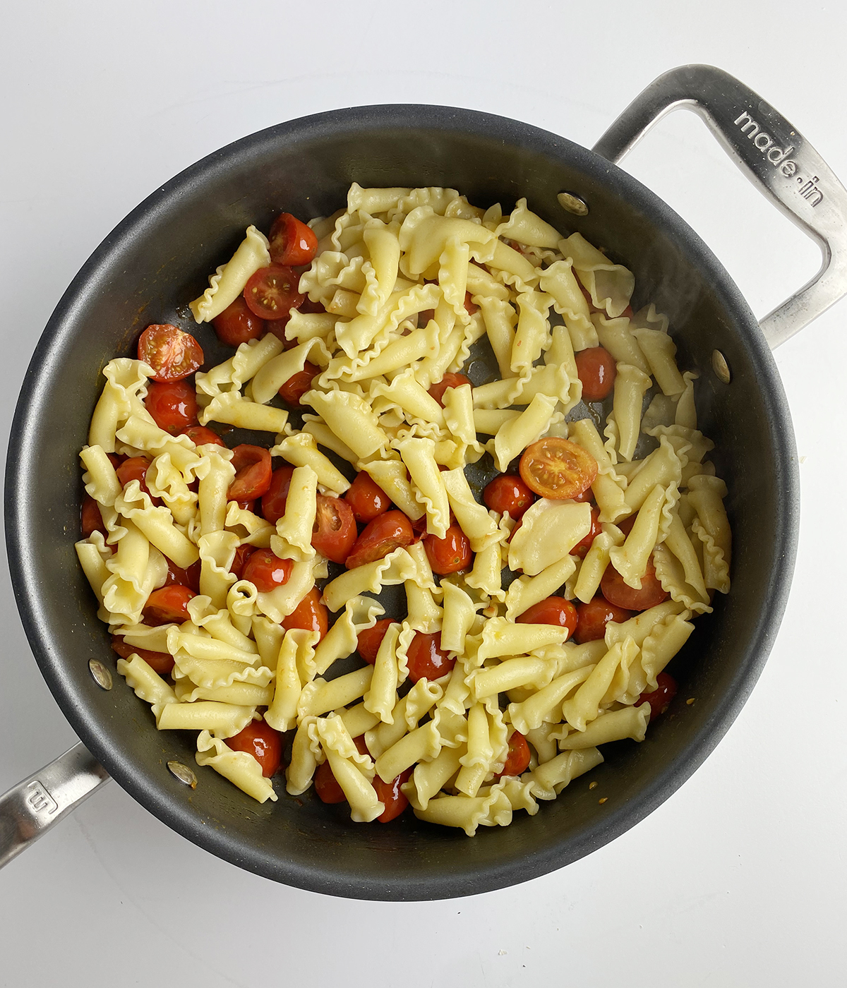 Pasta with cooked cherry tomatoes in a skillet.