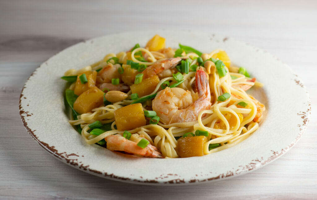 Pineapple Shrimp Noodles in a bowl on a wooden counter.