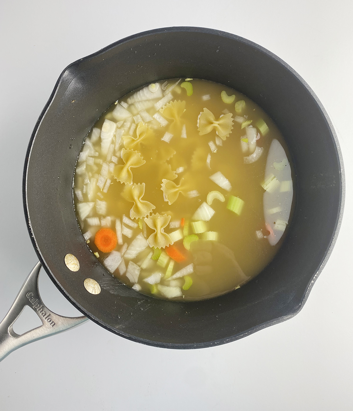 Veggies and broth for easy chicken noodle soup in a pot.