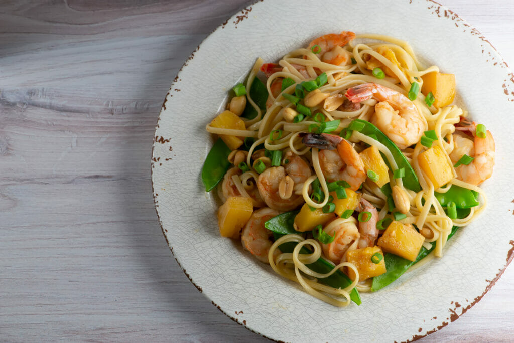 Pineapple Shrimp Noodles in a bowl on a wooden counter.