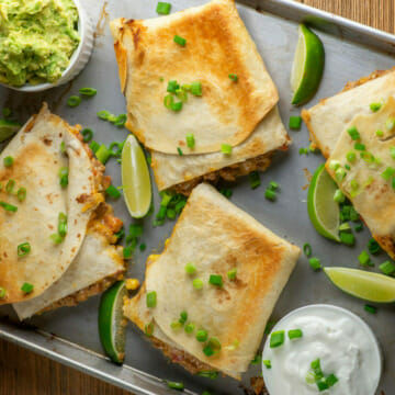 Sheet pan beef nacho quesadillas on a pan with guacamole and limes.