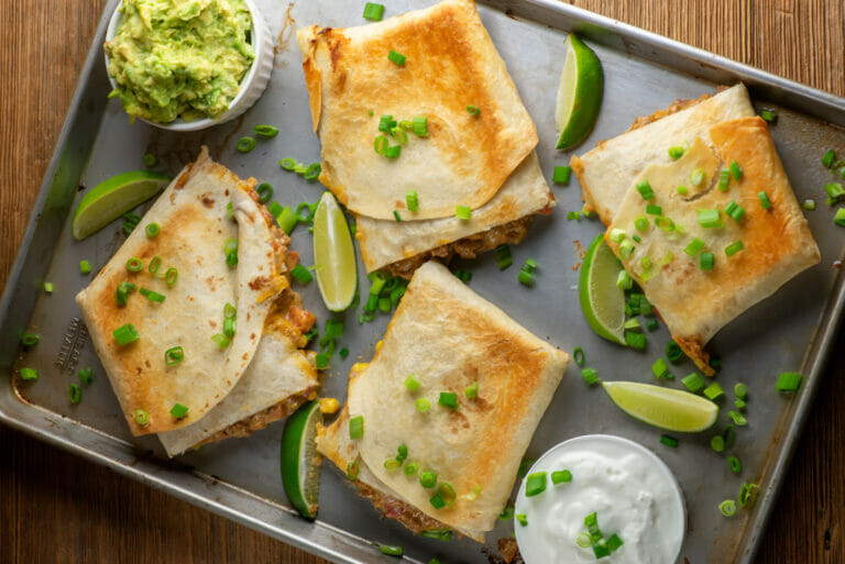 Sheet pan beef nacho quesadillas on a pan with guacamole and limes.