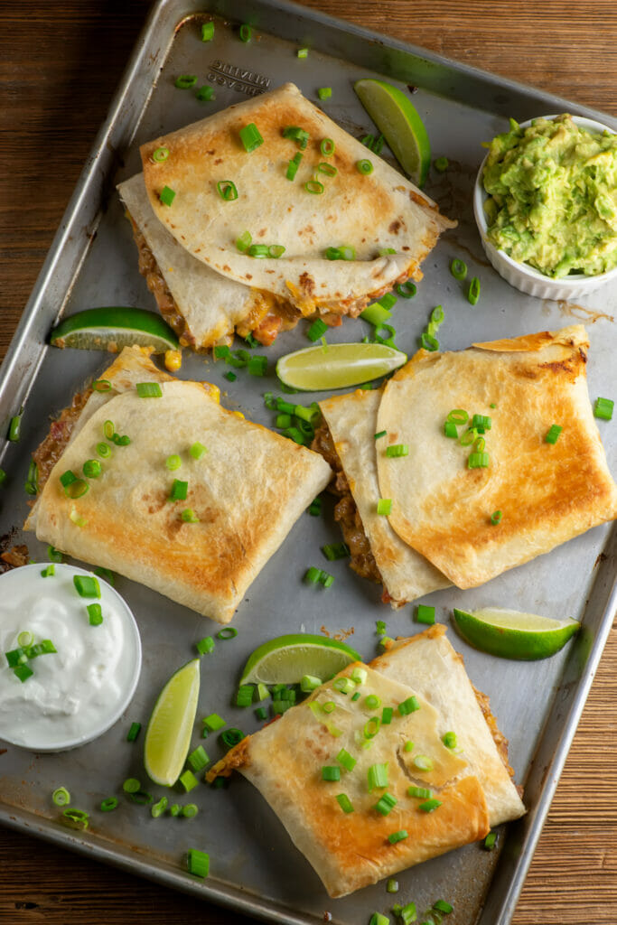 Sheet pan quesadillas on a pan with limes and guacamole.