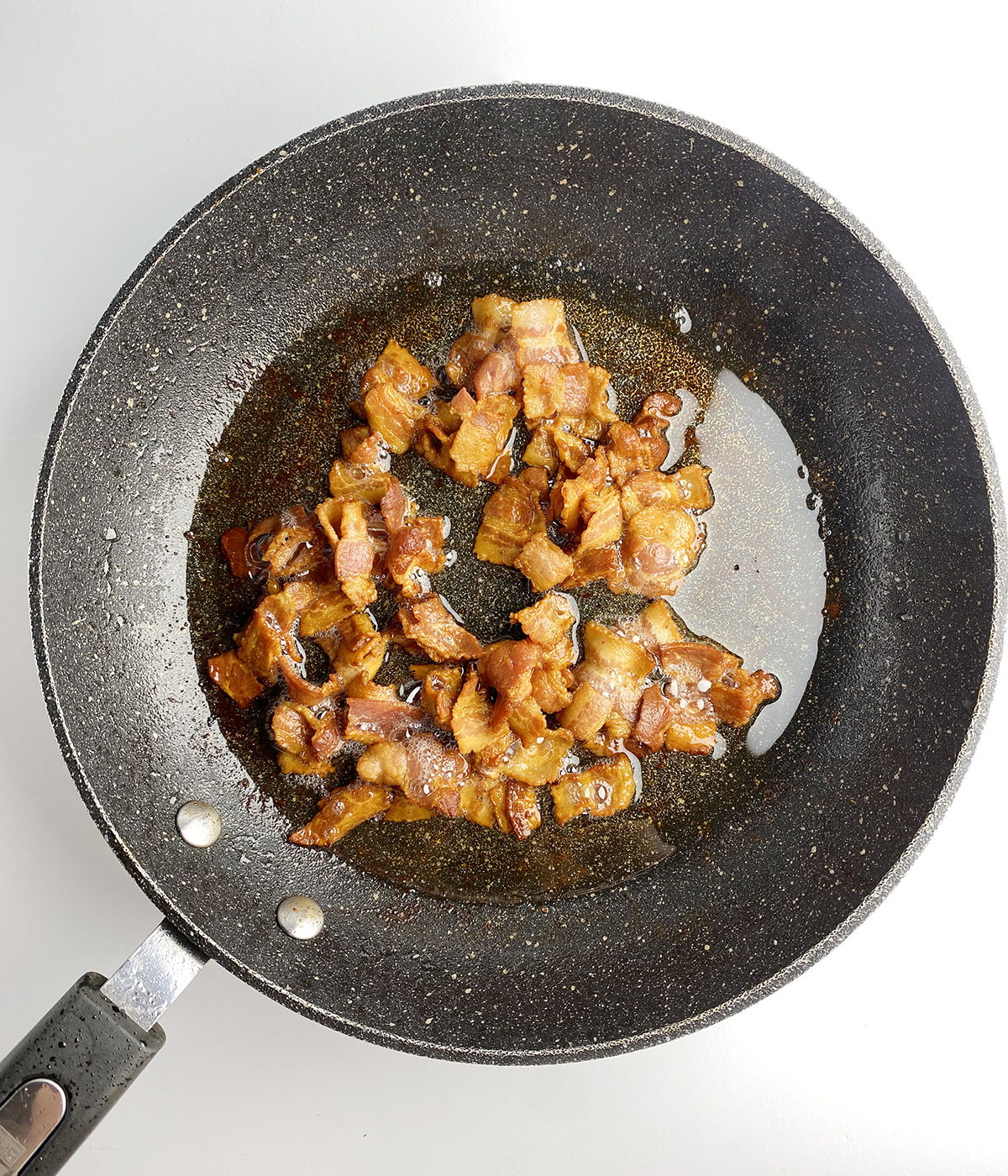 Chopped bacon cooking in a skillet.