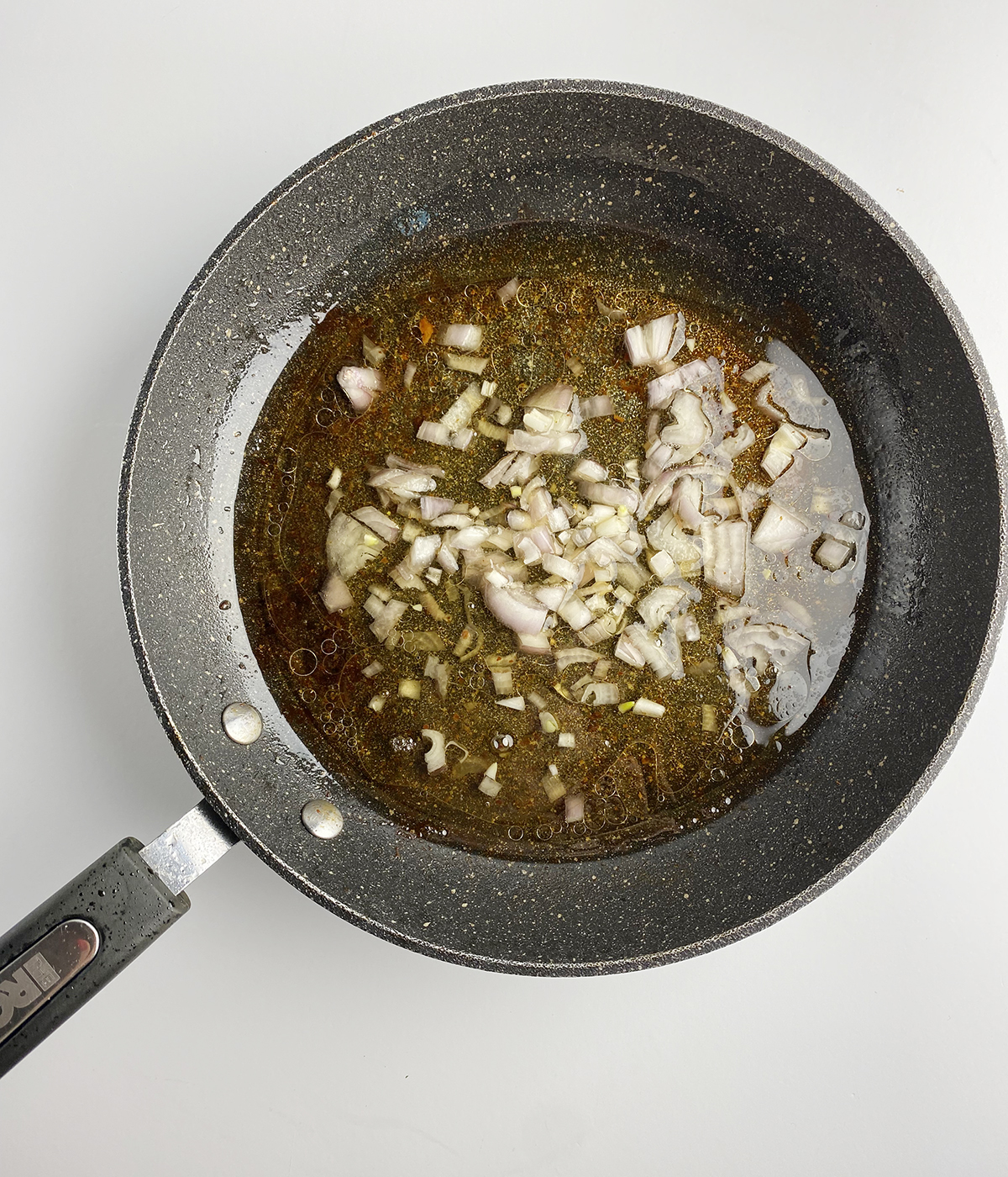 Shallots cooking in bacon drippings in a skillet.