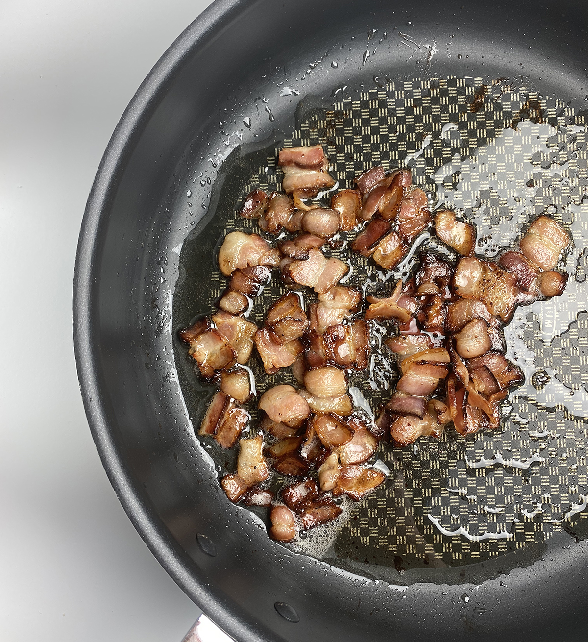 Chopped cooked bacon in a skillet with bacon drippings.