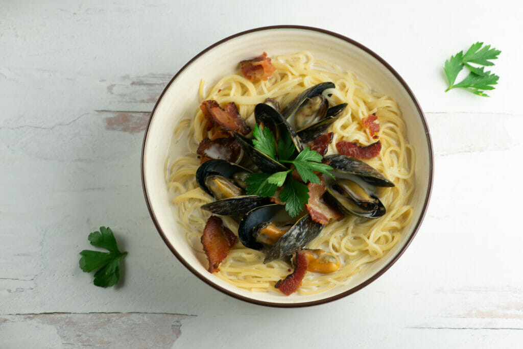 A bowl of creamy mussels in cider sauce on a bed of pasta.