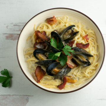 A bowl of creamy mussels in cider on a bed of pasta.