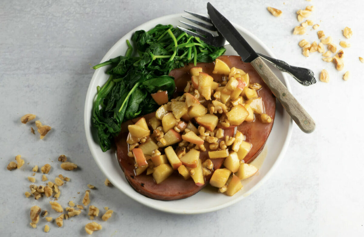 Finished recipe for ham steak with apples on a plate with a side of spinach.