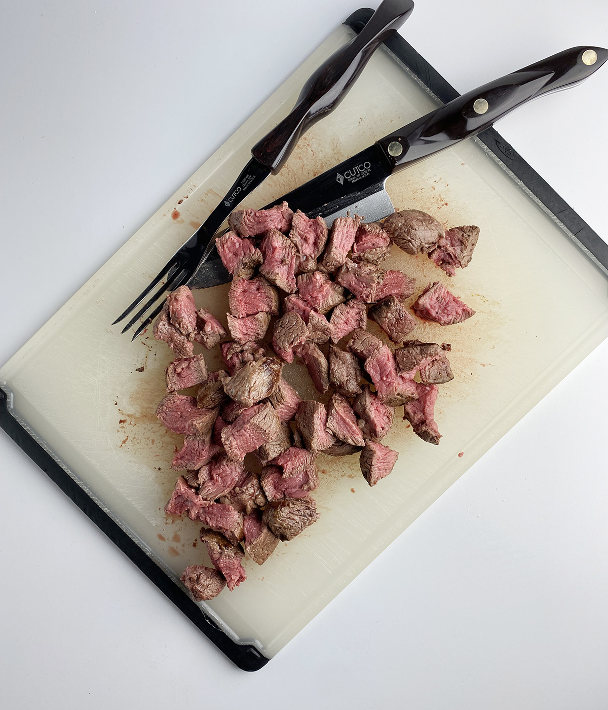 Chopped cooked filet mignon with knife and fork on a cutting board.