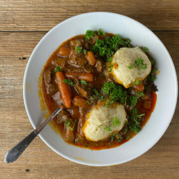 Beef Dumpling Stew on a bowl with a spoon on a wooden board.