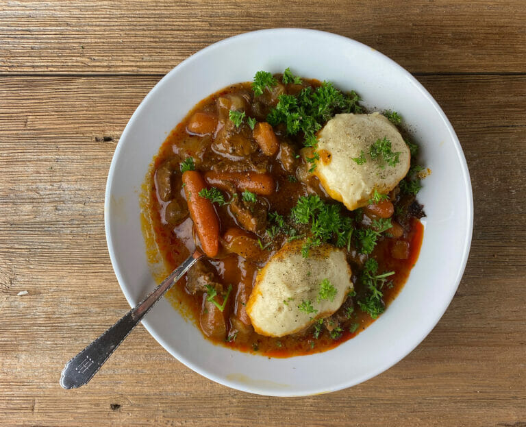Beef Dumpling Stew on a bowl with a spoon on a wooden board.