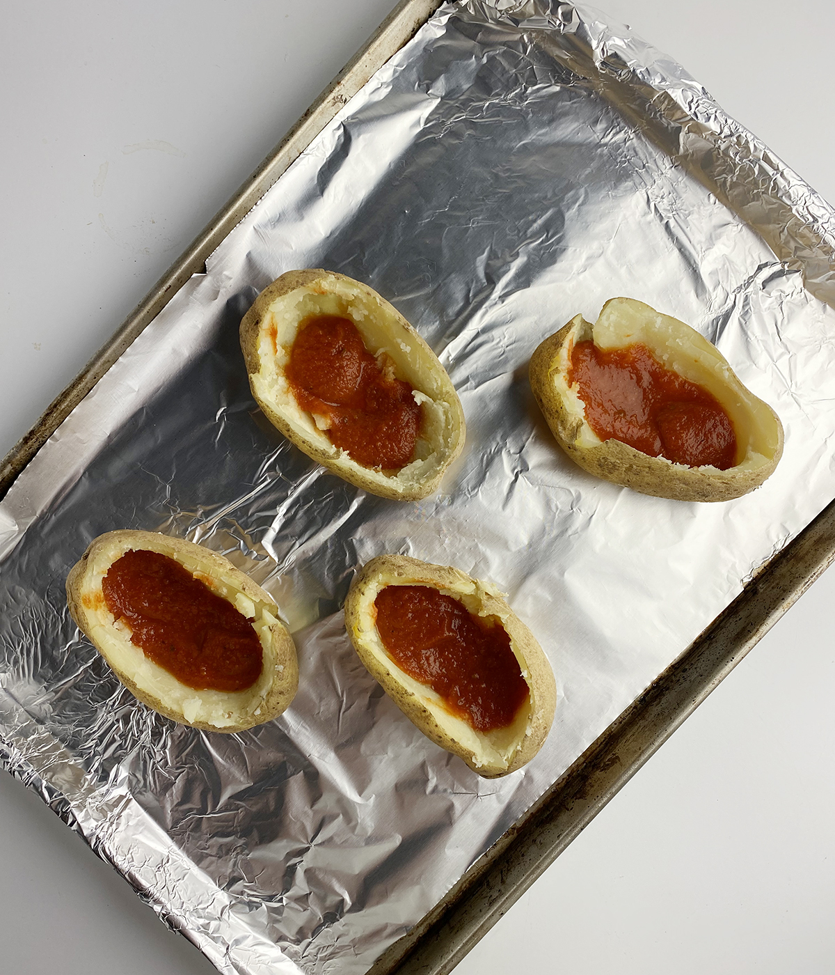 Potato skins with pizza sauce on a baking tray.
