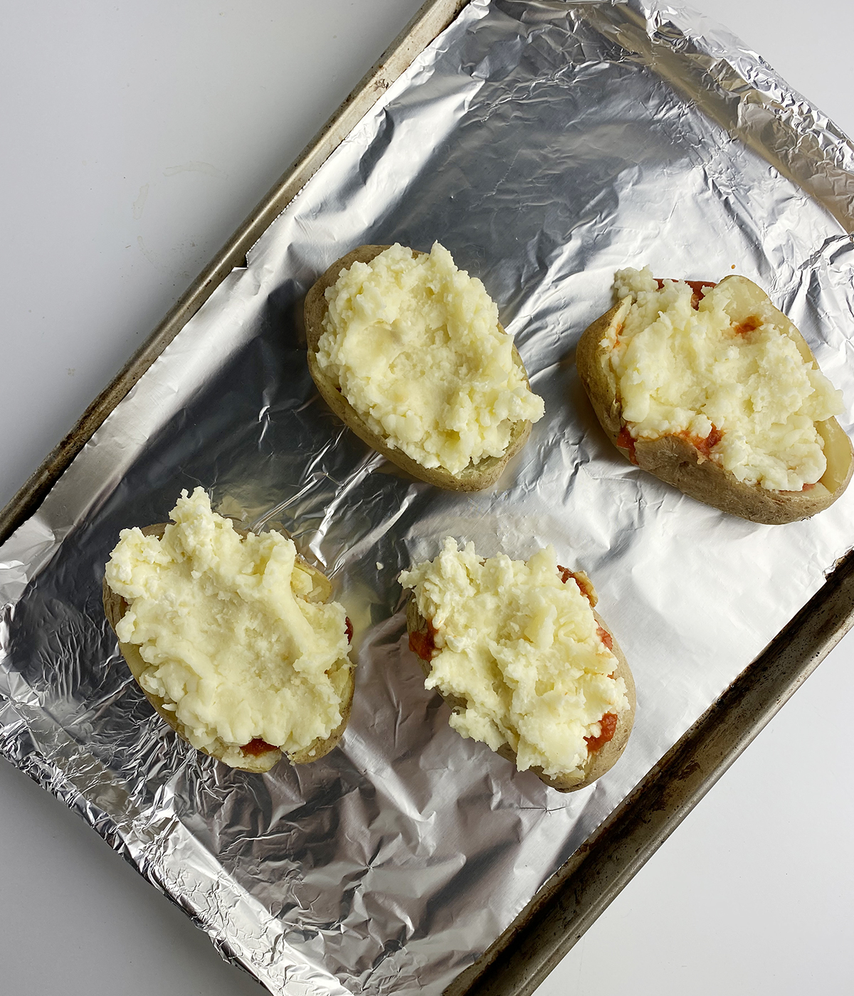 Potatoes stuff with mashed potatoes on a baking tray.