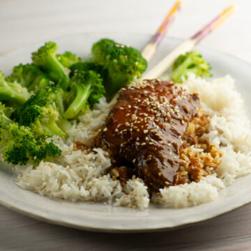 Slow cooker sticky chicken on a plate with rice and broccoli.