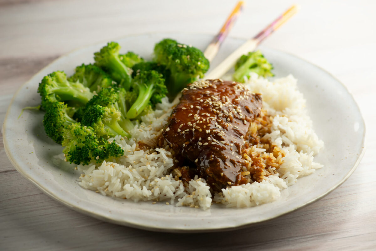 Slow cooker sticky chicken on a plate with rice and broccoli.