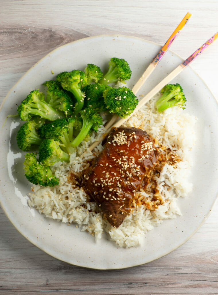 Slow cooker sticky chicken on a plate with broccoli and rice on the side.