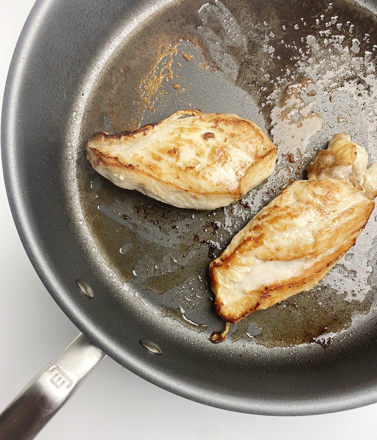 Chicken breasts browning in a skillet.