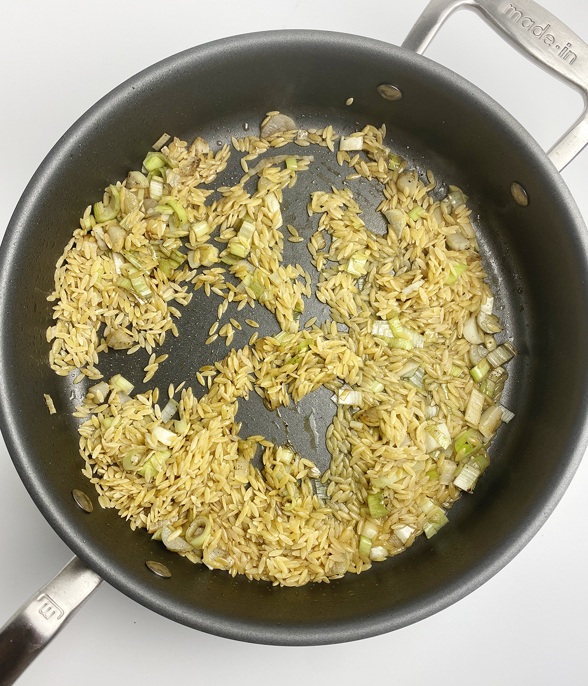 Orzo and leeks and wine cooking in a skillet.