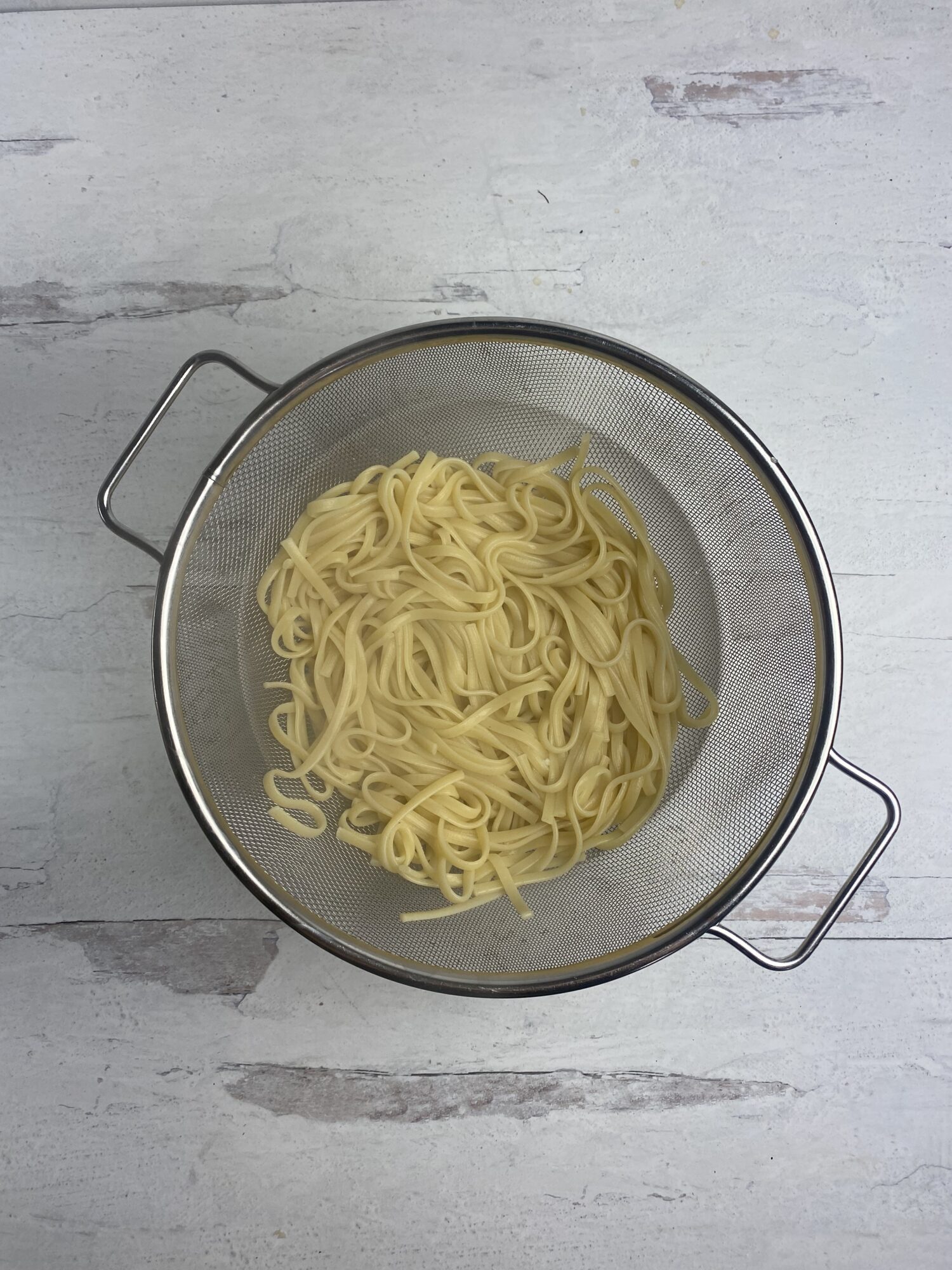 Cooked pasta draining in a metal colander.