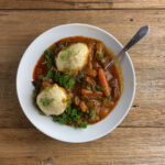 Bowl of beef dumpling stew on a wooden counter.