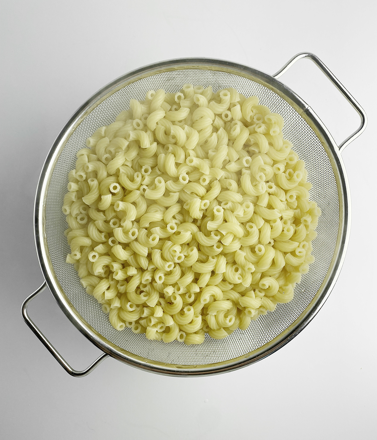 Elbow macaroni draining in a strainer.