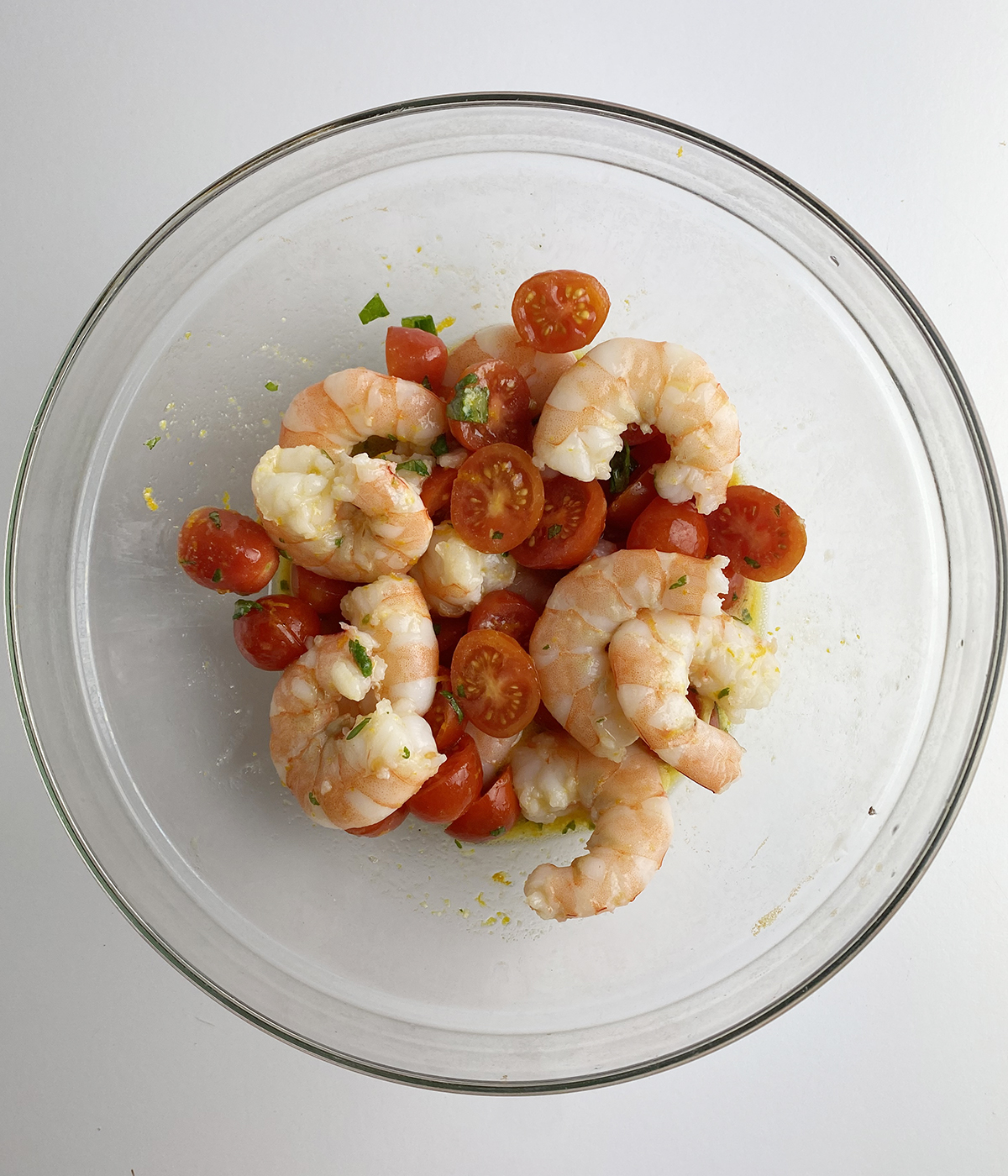 Shrimp, tomatoes and dressing tossed in a mixing bowl.